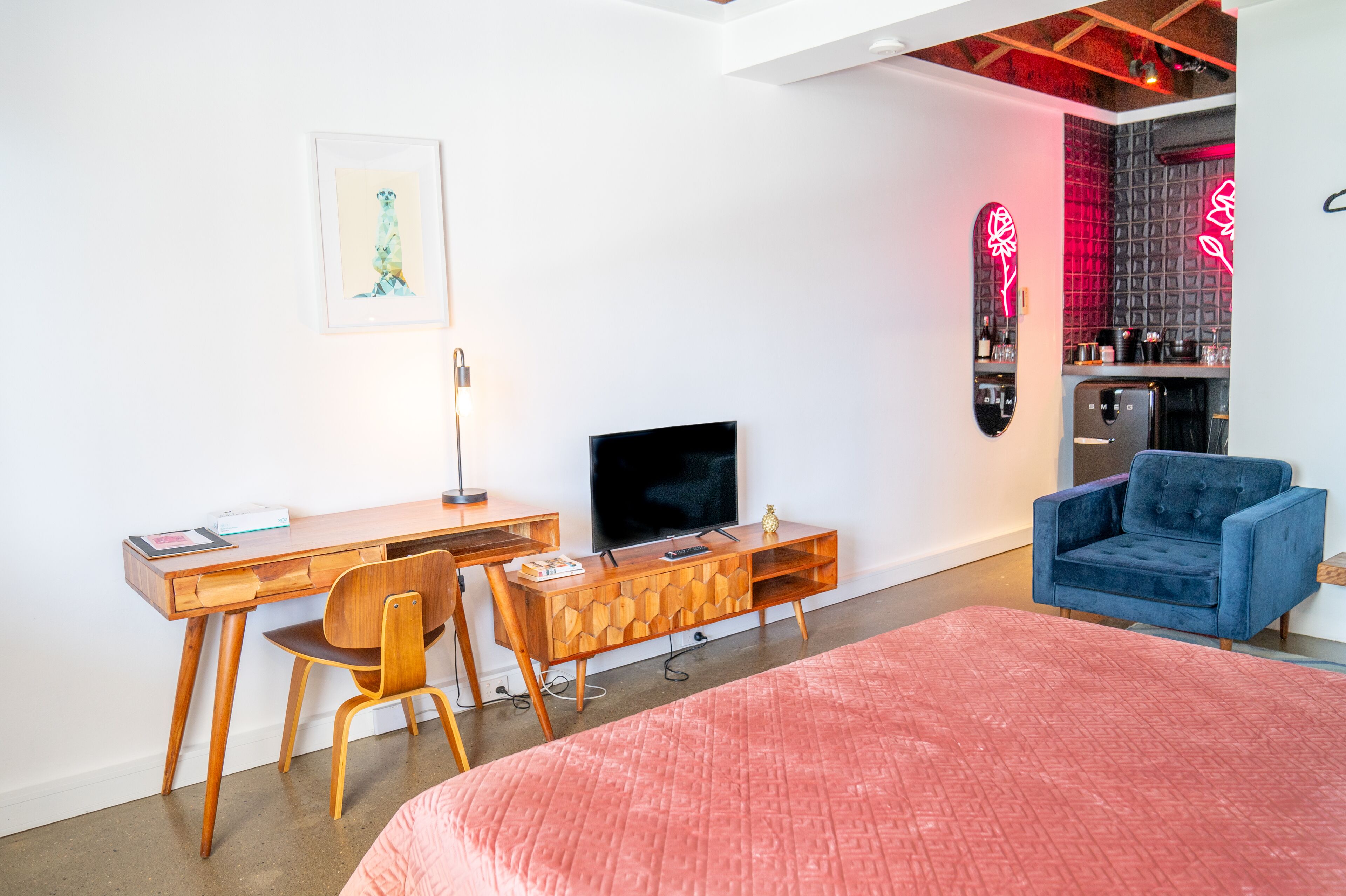 Ein modernes Schlafzimmer mit einem hölzernen Schreibtisch, einem Fernseher, einem blauen Sessel und einem Bett mit einer rosa Steppdecke.