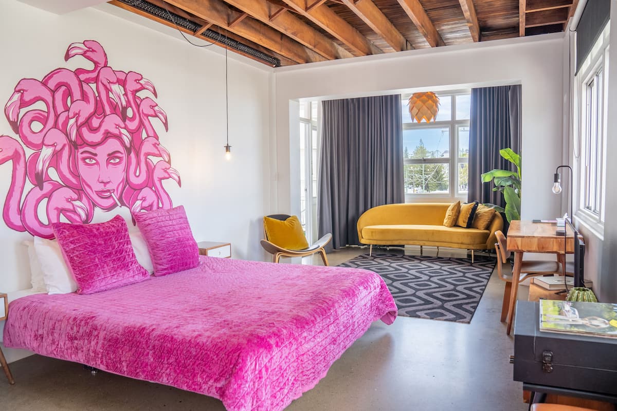 Een slaapkamer met een groot bed, een gele bank en een houten plafond.
