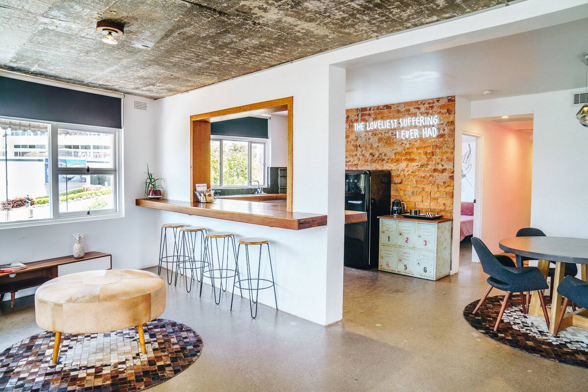 Een moderne keuken met een accentmuur van baksteen, een bar en een eethoek met krukken.