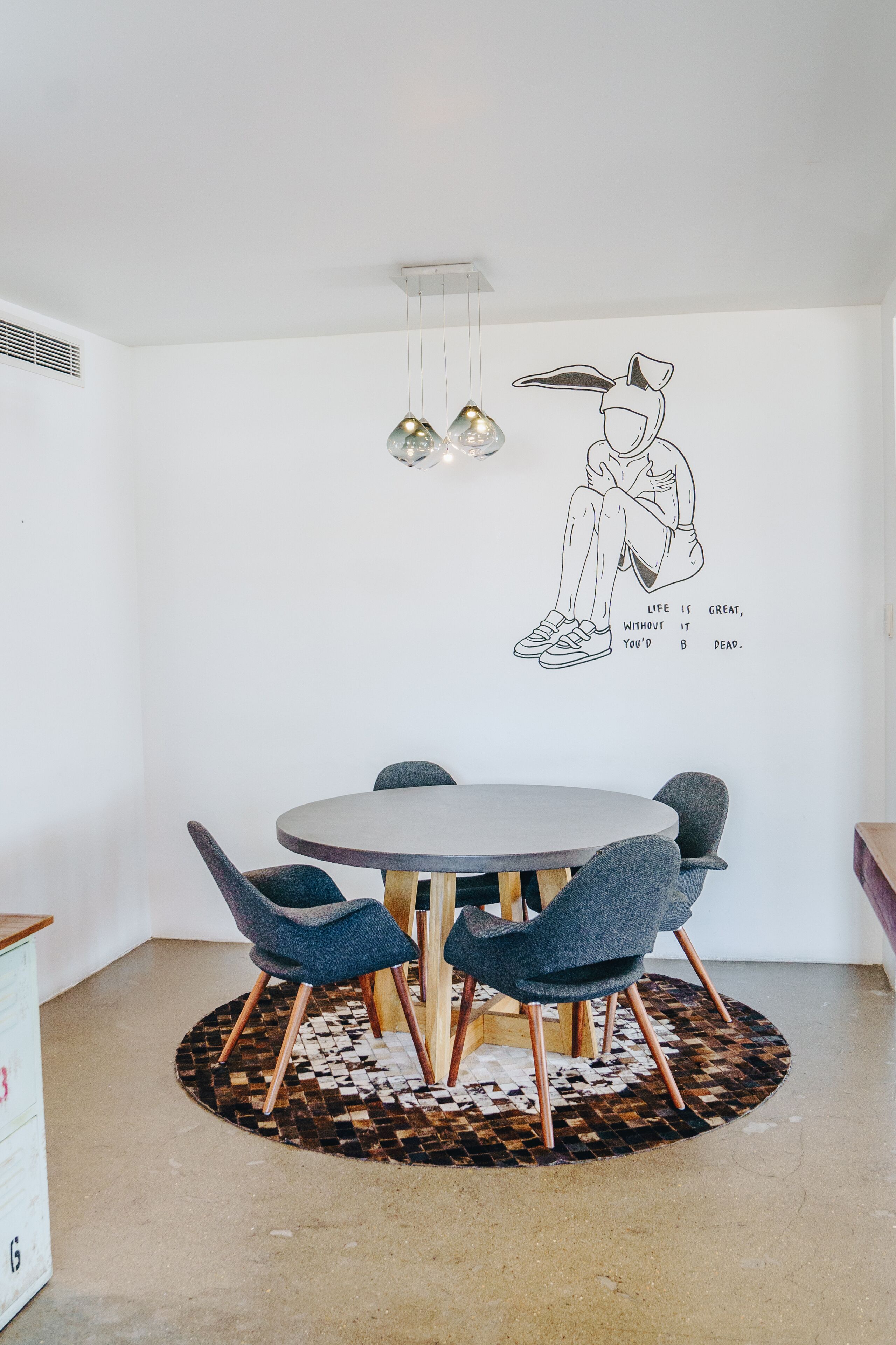 A dining area with a round table, four chairs, a wall mural, and pendant lighting.
