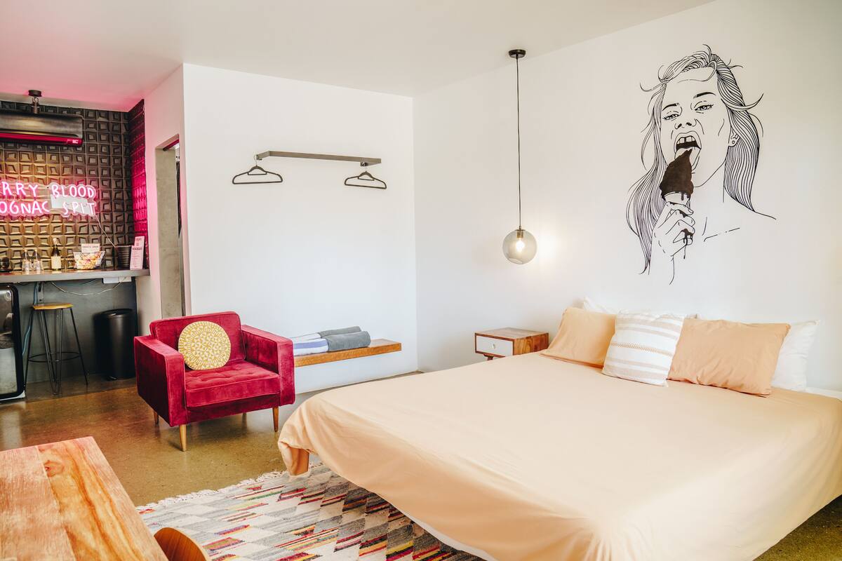 Een moderne slaapkamer met een groot bed, een rode stoel, een hanglamp en een neonbord.