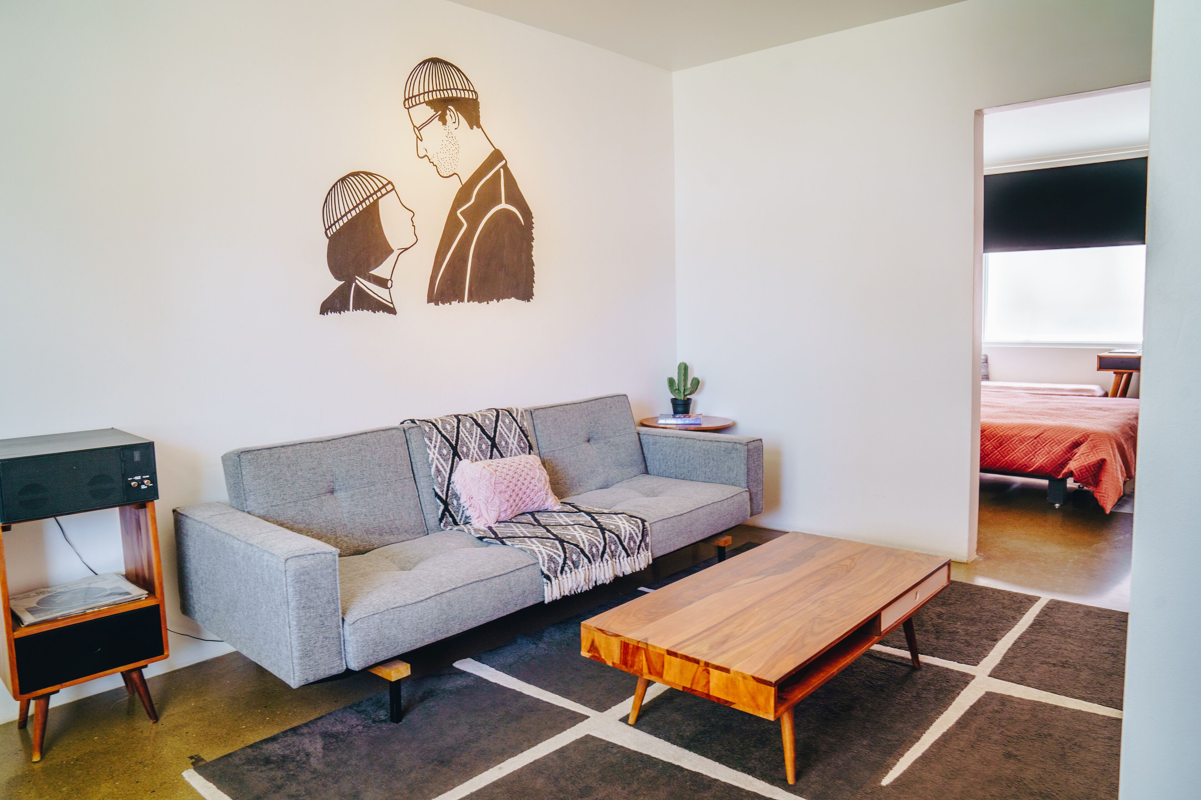 A modern living room with a grey sofa, a wooden coffee table, and a wall art depicting two people.