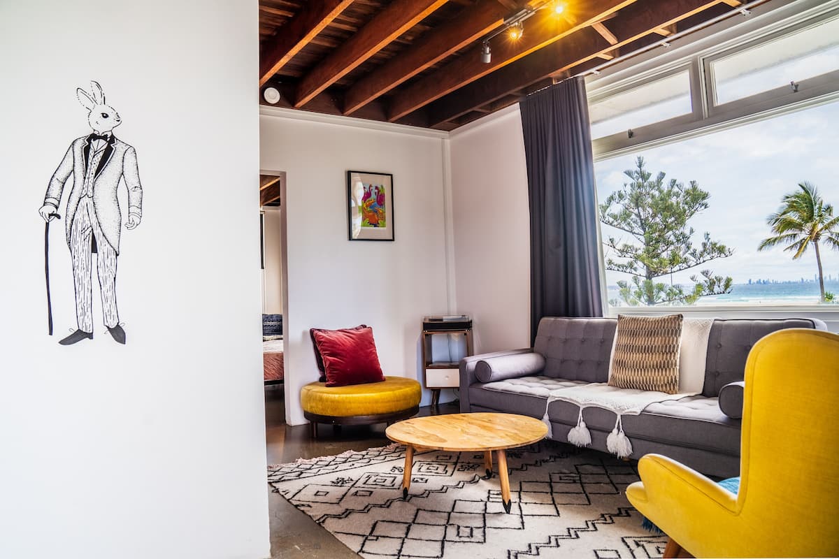 Een moderne woonkamer met een bank, een gele fauteuil en een ronde houten salontafel.