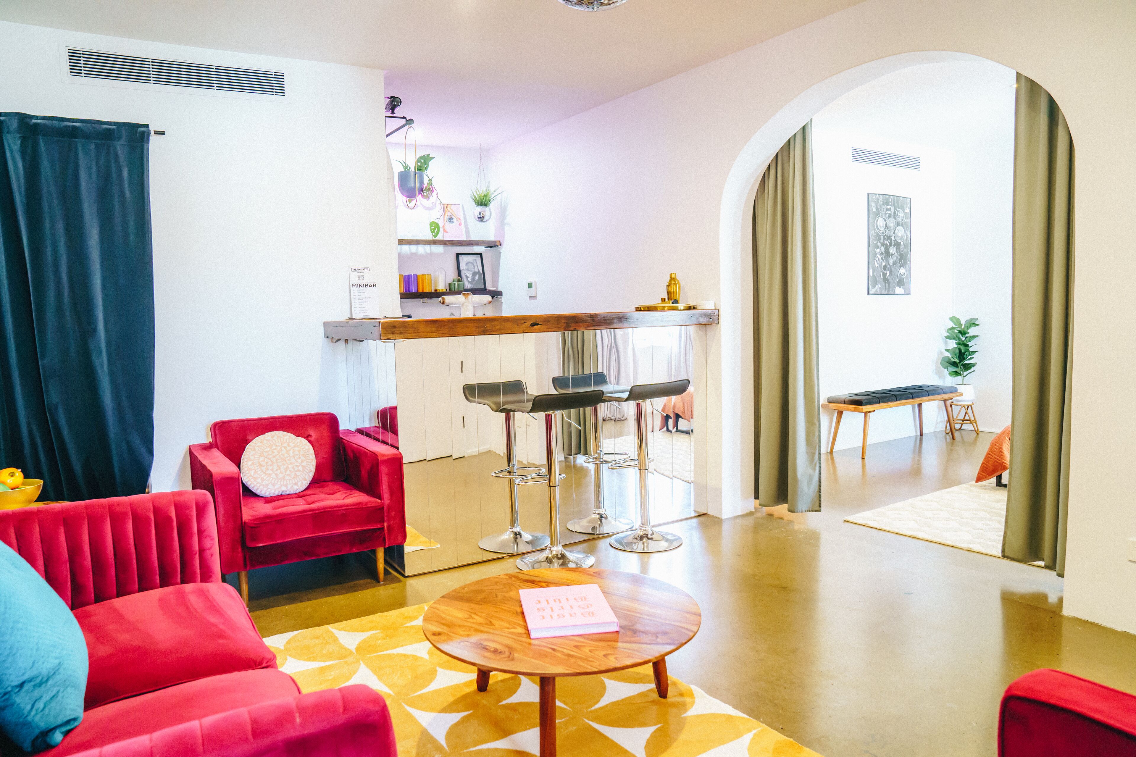 A modern living room with red sofas, a wooden coffee table, and a kitchen area in the background.