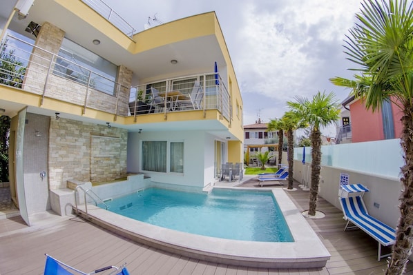 A two-story building with a swimming pool, outdoor seating, and a balcony.