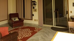 A living room with a red patterned rug, a brown leather armchair, a wooden coffee table, a sliding glass door, and a compass wall decoration. - Forks & twilighters getaway at the edge of SolDuc River.. bike, hike, walk, fish (Forks)