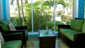 Una habitación con un gran ventanal corredero, mobiliario de mimbre y una pequeña mesa con un modelo de barco.