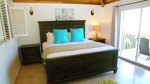 Un dormitorio con una cama grande, una mesita de noche, una lámpara, una ventana con persianas y vistas al exterior.