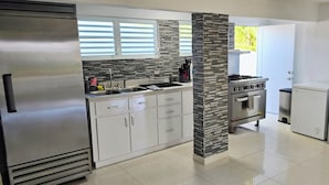 Una cocina moderna con armarios blancos, un refrigerador de acero inoxidable, una estufa a gas y una cafetera.