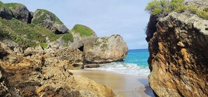 A rocky coastal landscape with a narrow passage between large boulders leading to a sandy beach.