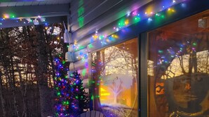 Una terrassa de fusta amb dues cadires Adirondack i una taula petita, decorada amb llums de colors i un arbre de Nadal.