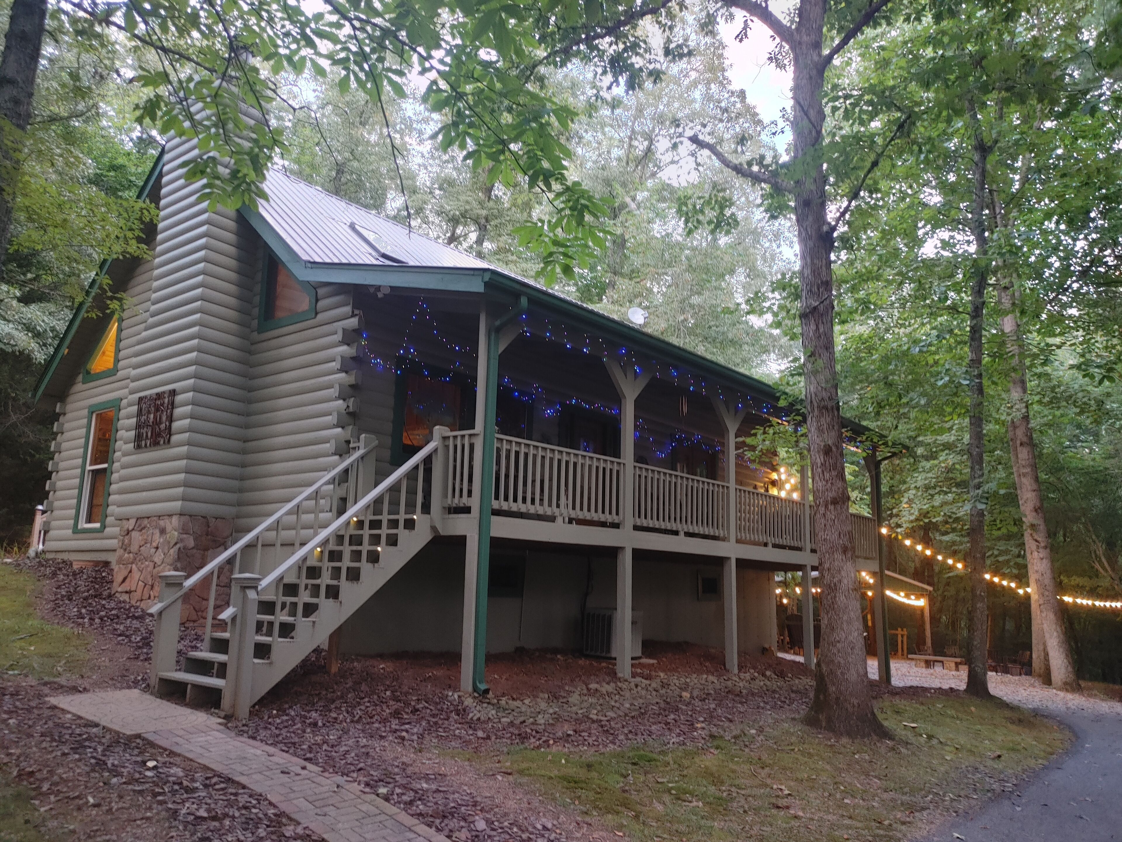 A log cabin with a porch and stairs, surrounded by trees.