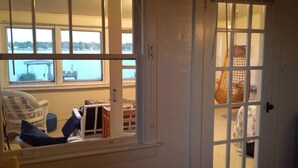 Habitación con vista a un muelle y al agua, un sillón de mimbre, una mesita y una puerta con diseño de cuadrícula.