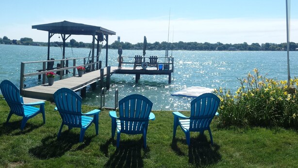 Una terraza junto al lago con sillas azules y una mesa, un área de descanso cubierta y un muelle que se extiende al agua.