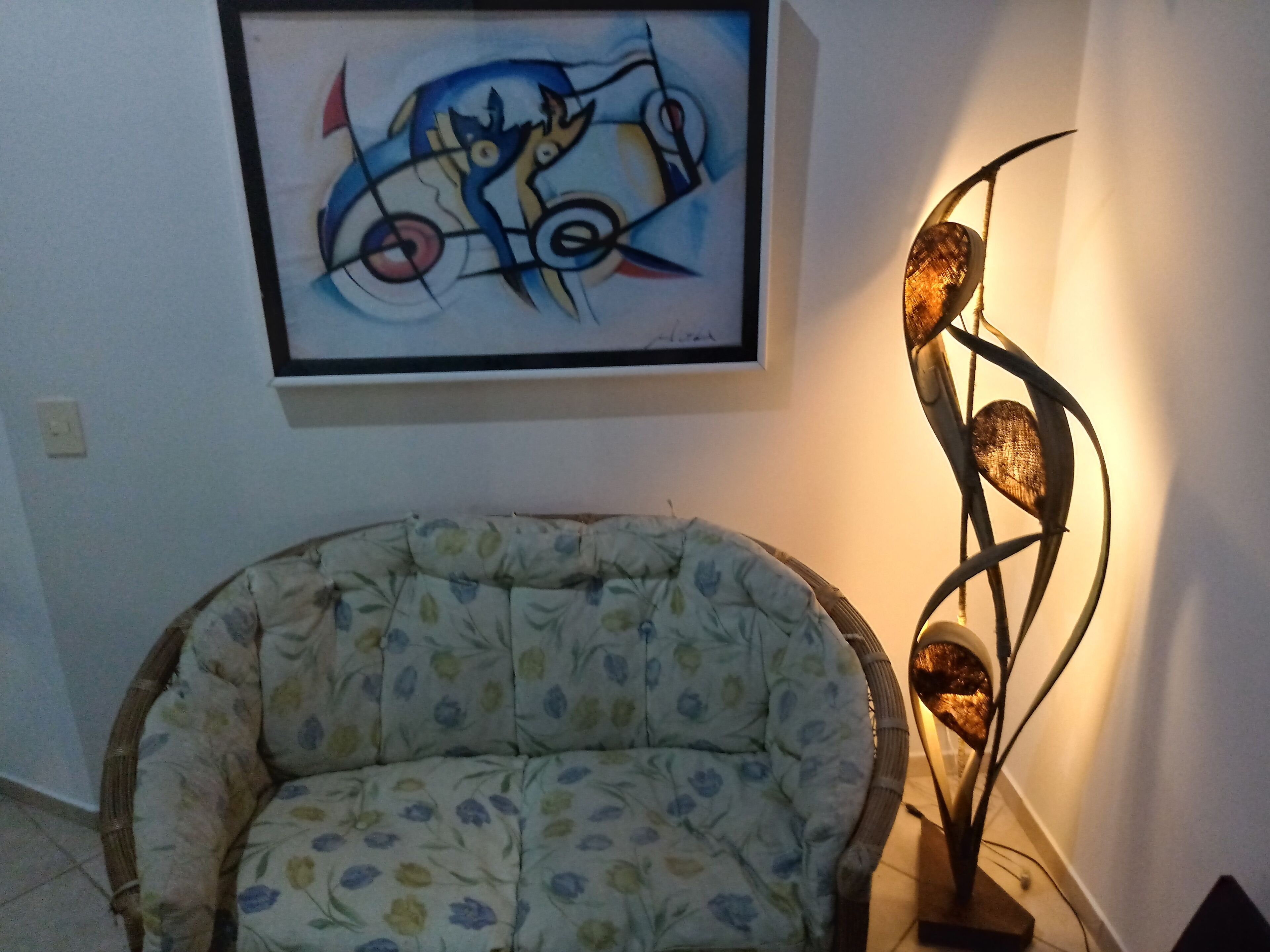 Una habitación con un sillón de estampado floral, un cuadro abstracto enmarcado y una lámpara de pie moderna.