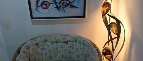 Una habitación con un sillón de estampado floral, un cuadro abstracto enmarcado y una lámpara de pie moderna.
