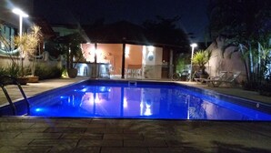 Una piscina con borde de azulejos, rodeada por una zona pavimentada con sillas y mesas.