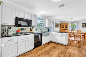 A modern kitchen with white cabinetry, a black microwave, and a wooden dining area.