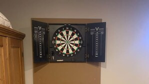 A dartboard mounted on a wall with a wooden cabinet to the left. - Ladies Castle on Main; 14 Beds (Fredericksburg)