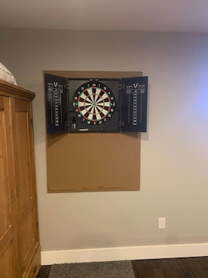 A dartboard mounted on a wall with a wooden cabinet to the left. - Ladies Castle on Main; 14 Beds (Fredericksburg)