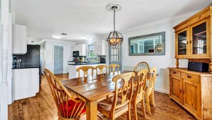 Una cocina amplia con armarios blancos, una mesa de comedor de madera con sillas, y un mueble grande de madera con puertas de vidrio.