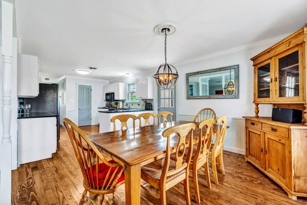 A spacious kitchen with white cabinets, a wooden dining table with chairs, and a large wooden cabinet with glass doors. - Ladies Castle on Main; 14 Beds (Fredericksburg)
