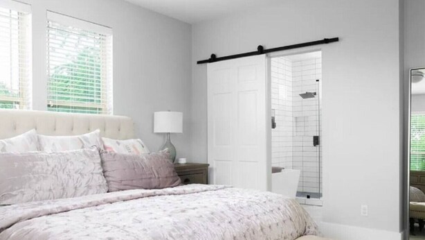 Un dormitorio con cama, mesita de noche, lámpara y una puerta corredera que da al baño.