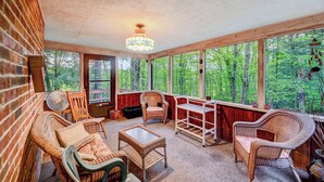 Ein gemütliches Zimmer mit Rattanmöbeln, einem Deckenventilator und großen Fenstern mit Blick auf den Wald.