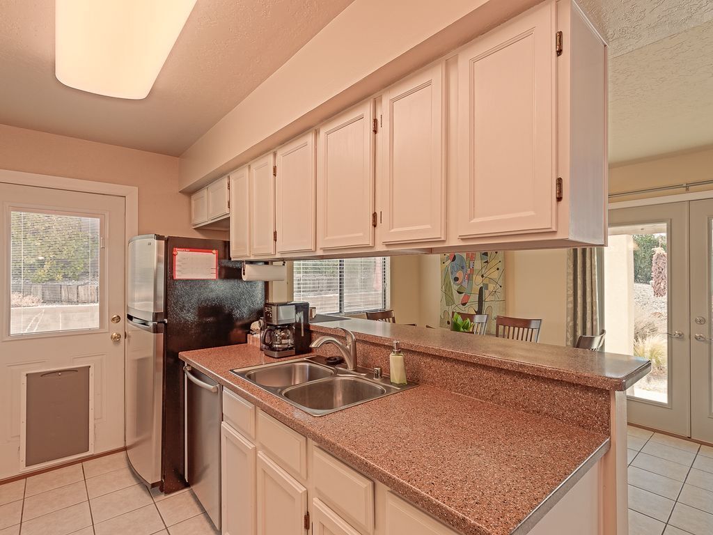 A kitchen with white cabinets, a granite countertop, stainless steel appliances, and a window with blinds.