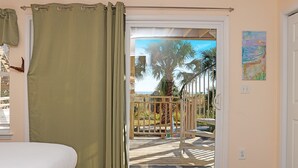 A bedroom with a bed, a sliding glass door leading to a balcony with a view of palm trees and a wooden deck. - Pool, Gulf Front, Great Views ~ Gulfside GEM (Indian Pass)