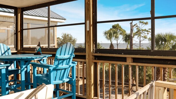A covered outdoor area with blue Adirondack chairs and a wooden table, overlooking a beach with palm trees and a clear sky. - Pool, Gulf Front, Great Views ~ Gulfside GEM (Indian Pass)