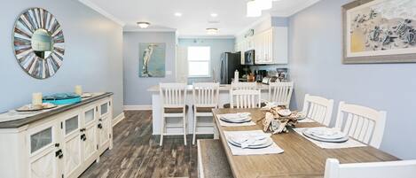 A dining area with a wooden table, white chairs, and a kitchen in the background.