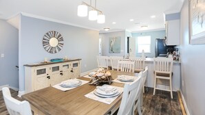 A dining area with a wooden table set for six, white chairs, a chandelier, and a decorative wall piece.