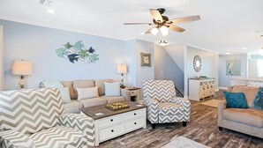 A living room with a sofa, armchairs, a coffee table, and a ceiling fan.