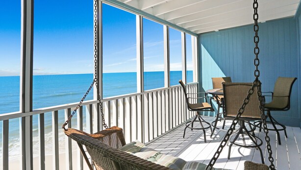 A covered outdoor area with a view of the ocean, wicker furniture, and a table with chairs.