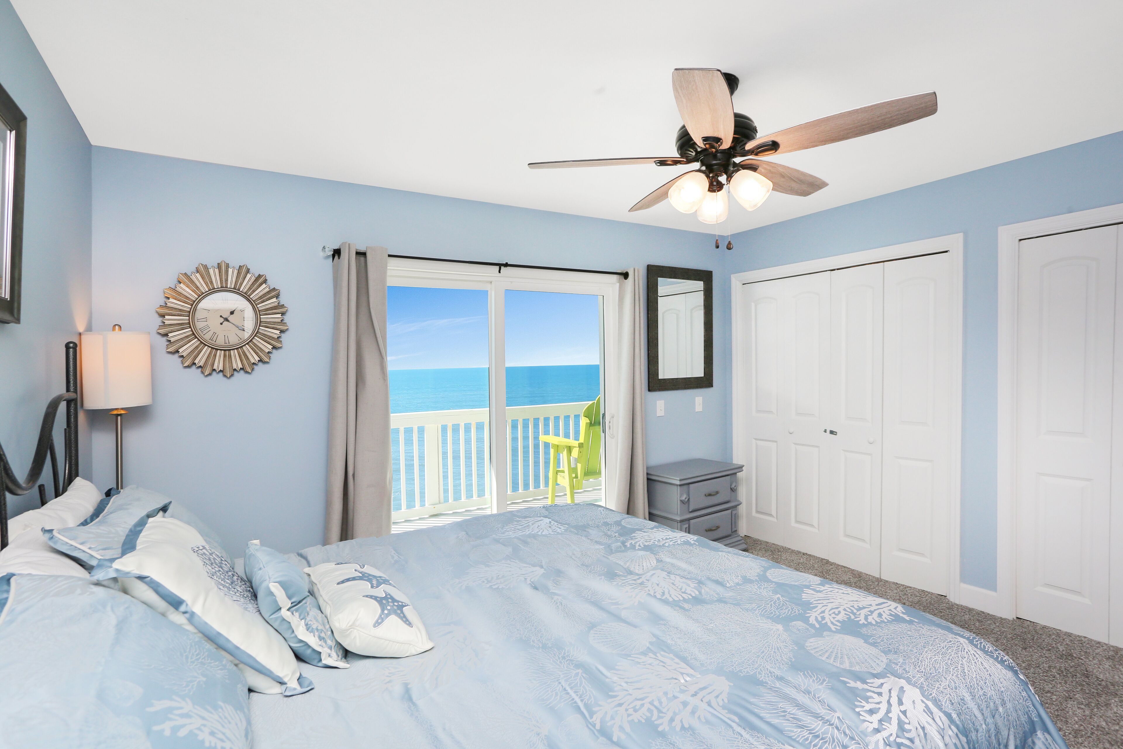 Un dormitorio con cama, ventilador de techo, reloj, ventana con vistas y puerta.