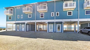 A two-story building with balconies, a covered parking area, and a view of the beach.