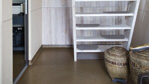 Huone, jossa on kalteva katto, seinään integroitu penkki hyllyineen, ovi, joka johtaa vaatehuoneeseen, ja kaksi rottinkikoria.