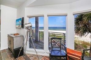 A balcony with a view of the ocean, a chair, a bench, and a tripod-mounted camera.