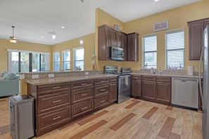 A kitchen with dark brown cabinets, granite countertops, stainless steel appliances, and a herringbone-patterned floor.