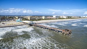 A pier extending into the ocean with a beach and buildings in the background. - SOL: pool, 1 blk to the beach. 3b/3.5ba. beach items, longbrd, picklball close (Cocoa Beach)