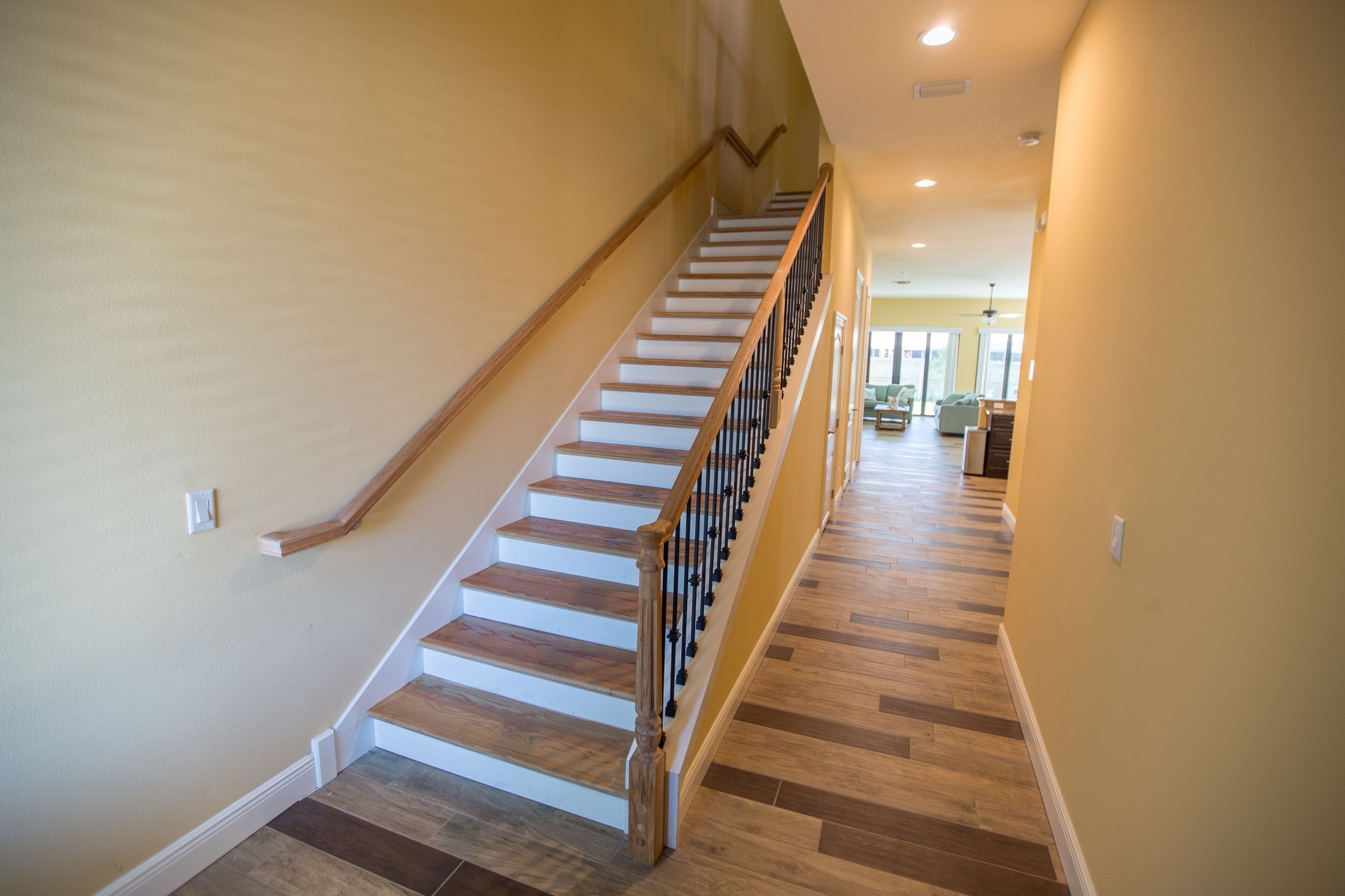 A staircase with wooden steps and a black railing, leading to a room with a large window and a ceiling fan.