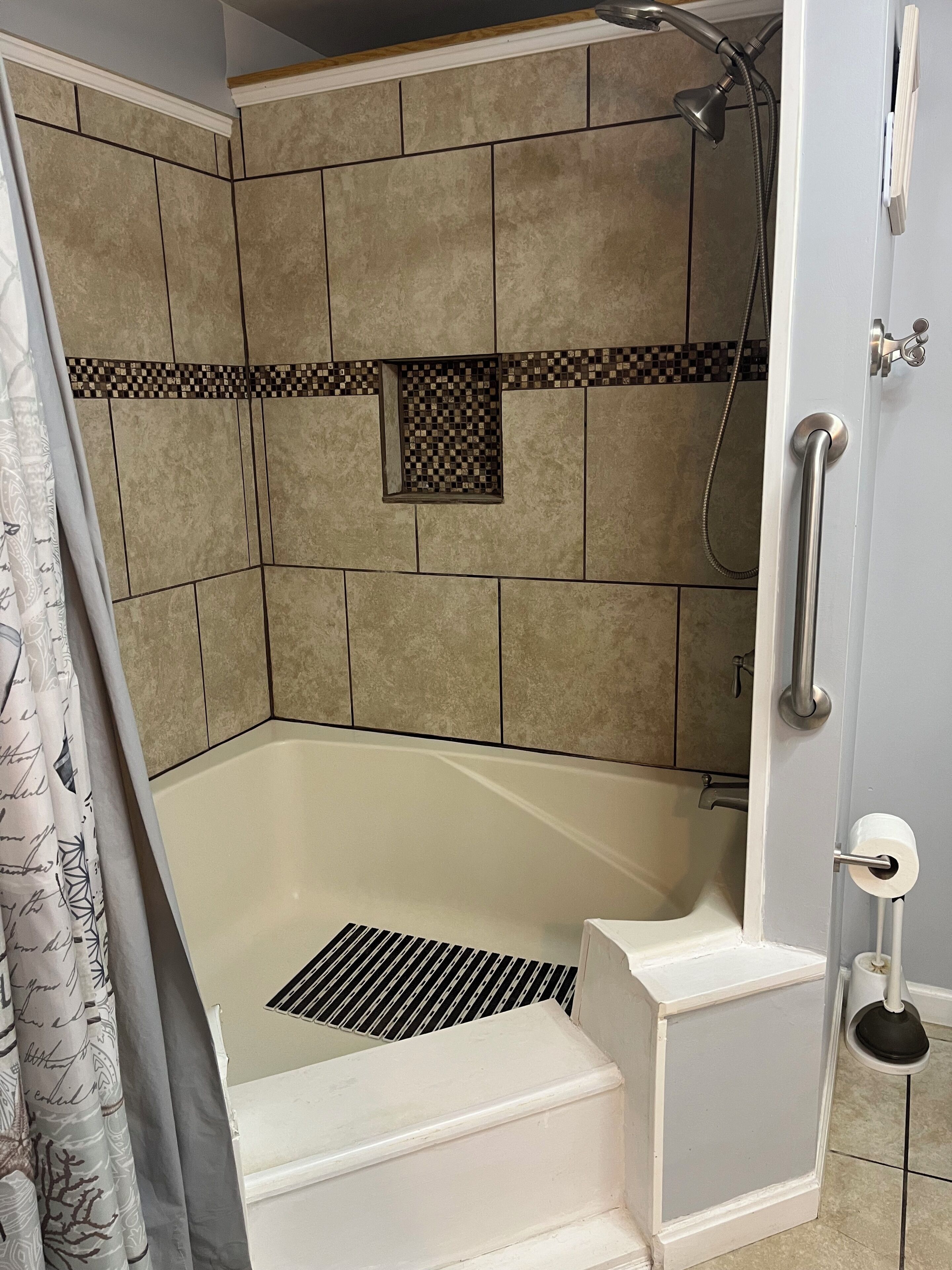Ducha en esquina con azulejos color beige, una bañera blanca y un cabezal de ducha.