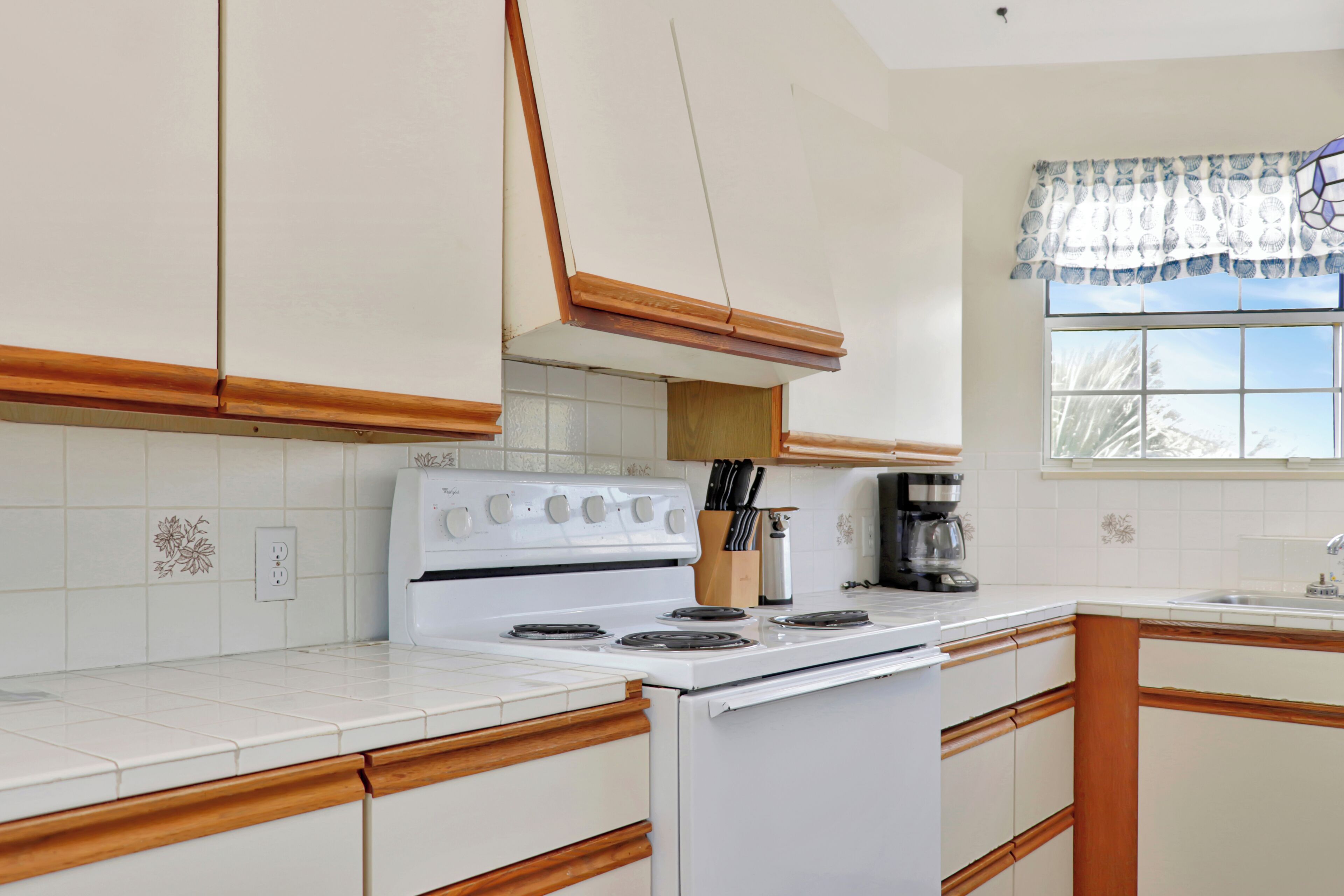A kitchen with white cabinets, a stove, and a window with a patterned valance.