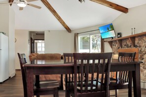 A dining area with a wooden table and chairs, a television on the wall, and a stone fireplace.