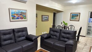 A living room with two black leather sofas, a glass coffee table, and a dining area with a glass table and chairs. - Apartment on the beachfront of Praia do Forte in Cabo Frio, opposite Praça das Águas. (Cabo Frio)