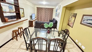 A dining area with a glass table and wooden chairs, a sofa, and a TV in the background. - Apartment on the beachfront of Praia do Forte in Cabo Frio, opposite Praça das Águas. (Cabo Frio)