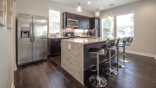 A modern kitchen with a stainless steel refrigerator, granite island, bar stools, and pendant lighting. - NEW Modern House with Roof Deck of Atlanta Skyline (Atlanta)