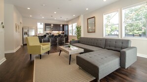 A modern living room with a gray sectional sofa, a yellow armchair, and a coffee table. There is a kitchen in the background with dark cabinets and a large window. - NEW Modern House with Roof Deck of Atlanta Skyline (Atlanta)