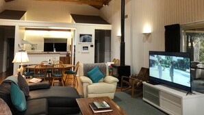 A spacious living room with a high ceiling and wooden beams, a television, and a dining area with chairs and a table. - Absolute  luxury, surprising additions, welcome hamper & wine, cheese & biscuits (Hunter Valley)